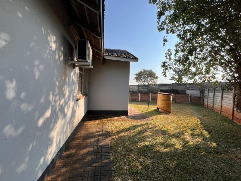 Rear exterior view of the property featuring a paved walkway, lawn area, and perimeter precast concrete walling.