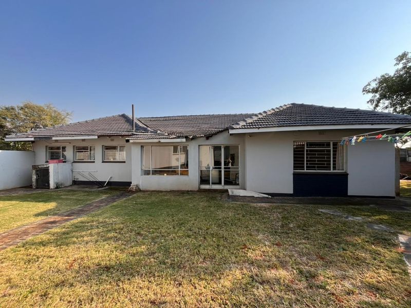 Rear view of a single-story house featuring a tiled roof, sliding glass doors, and a spacious garden with paved pathways.