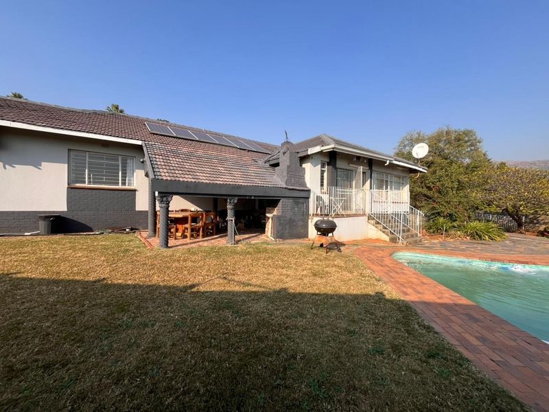 Rear view of the house featuring a covered patio with a built-in fireplace, swimming pool, and solar panels installed on the tiled roof.