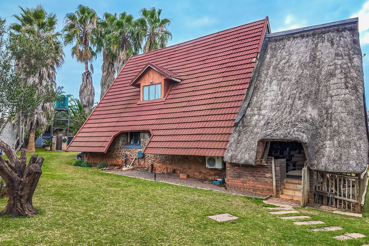 A unique A-frame style house featuring a combination of tiled and thatched roofing, stone and brick exterior walls, and a spacious surrounding garden.