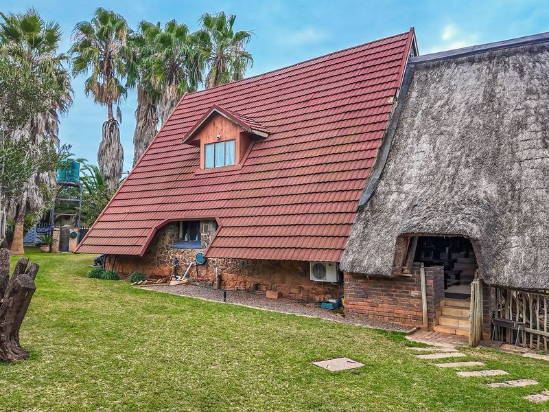 A unique A-frame style house featuring a combination of tiled and thatched roofing, stone and brick exterior walls, and a spacious surrounding garden.