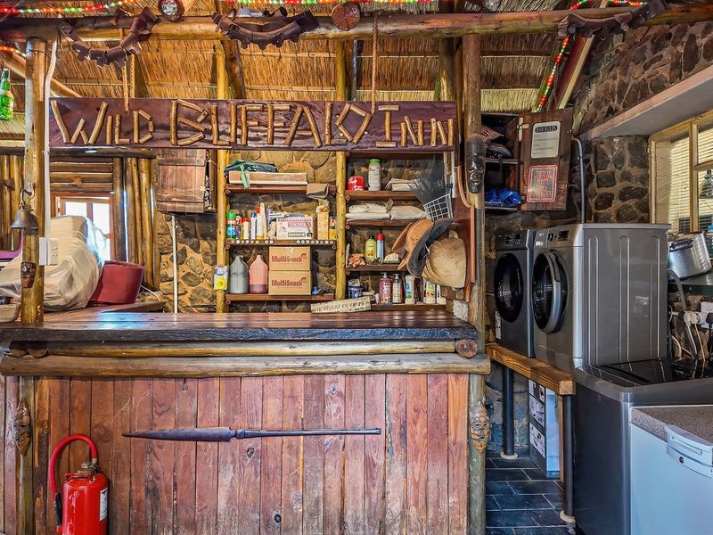 Rustic bar area featuring a thatched roof, stone walls, timber pole construction, and integrated laundry facilities with a wooden bar counter.
