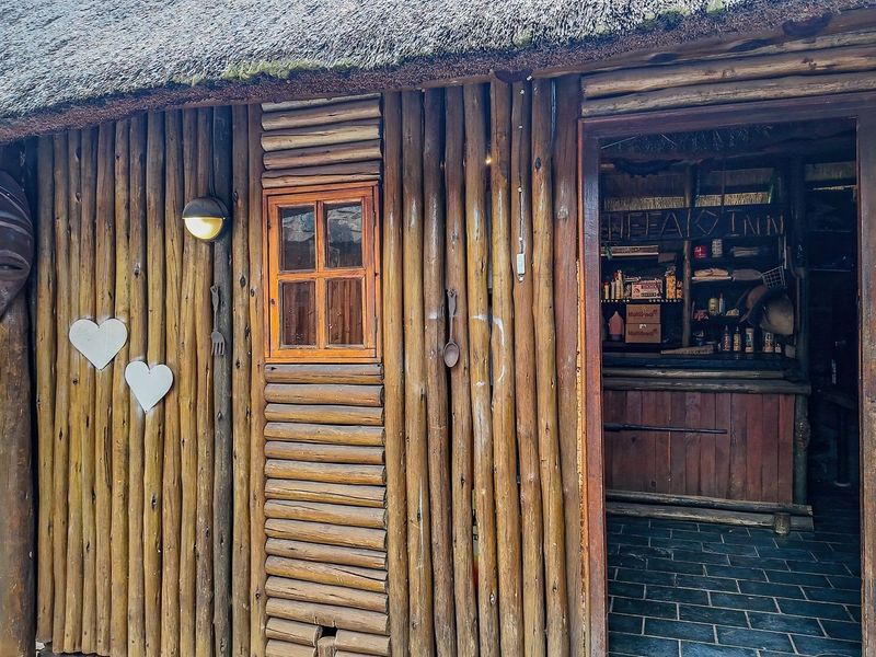 Rustic outdoor bar area featuring a thatched roof, log-clad exterior walls, and a built-in bar counter with slate flooring.