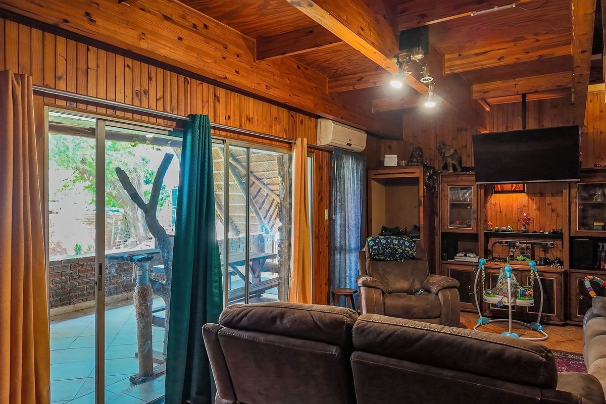 Cozy living room featuring warm timber wall paneling, exposed ceiling beams, and large sliding glass doors providing direct access to the outdoor patio area.