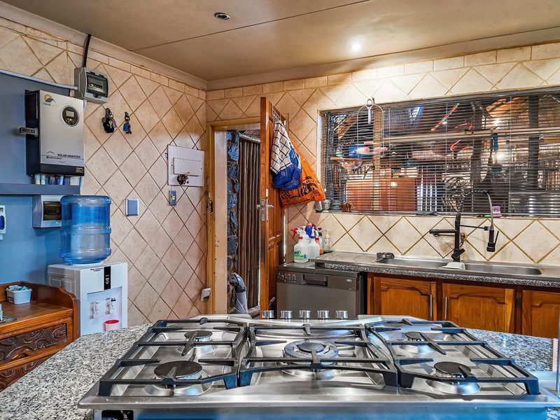 Functional kitchen featuring granite countertops, a gas hob, double sink, and integrated solar inverter system with wooden cabinetry and tiled backsplash.