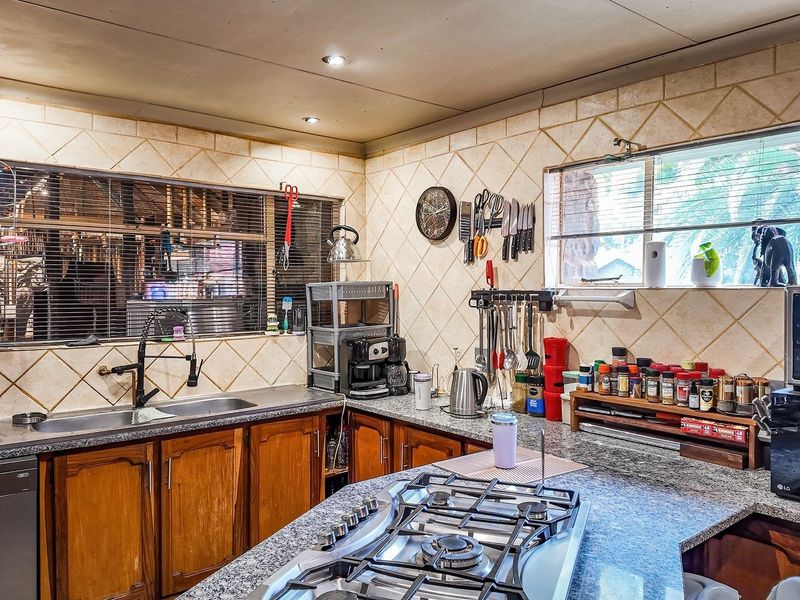 A functional kitchen featuring granite countertops, wooden cabinetry, a built-in gas hob, and a tiled backsplash with ample natural light.