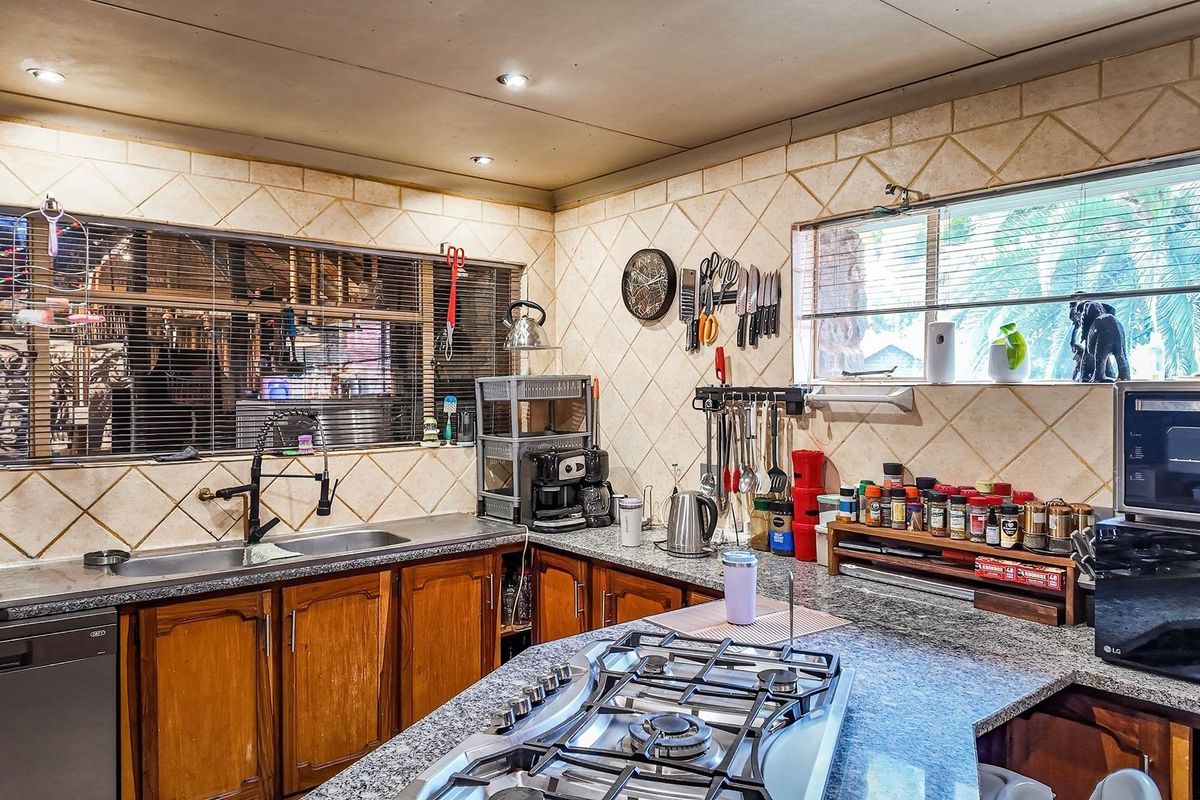 A functional kitchen featuring granite countertops, wooden cabinetry, a built-in gas hob, and a tiled backsplash with ample natural light.