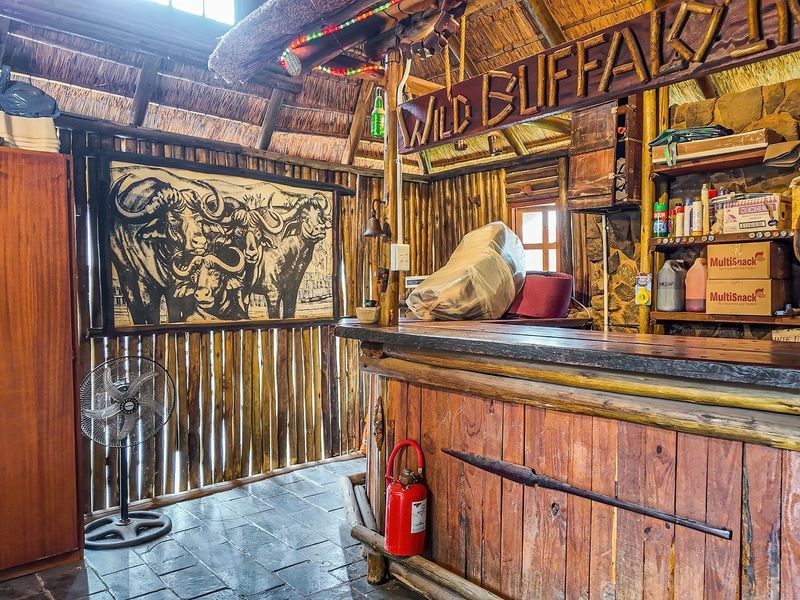 Rustic themed bar area featuring a built-in timber counter, traditional thatched roof, stone wall accents, and durable slate tile flooring.