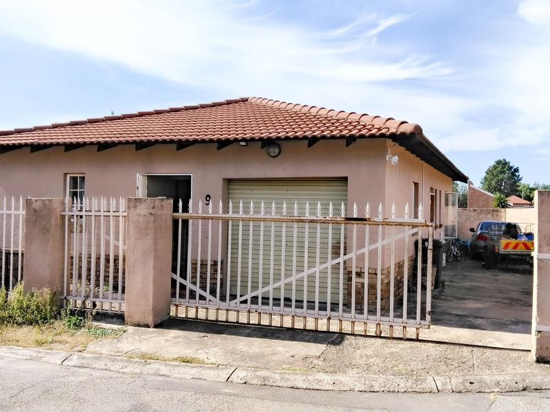 Front view of a single-story house featuring a tiled roof, roller garage door, and secure metal perimeter fencing with a driveway.