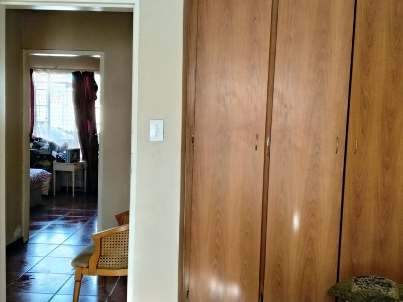 Bedroom featuring built-in wooden wardrobes and tiled flooring, with a view through the doorway into an adjacent room.