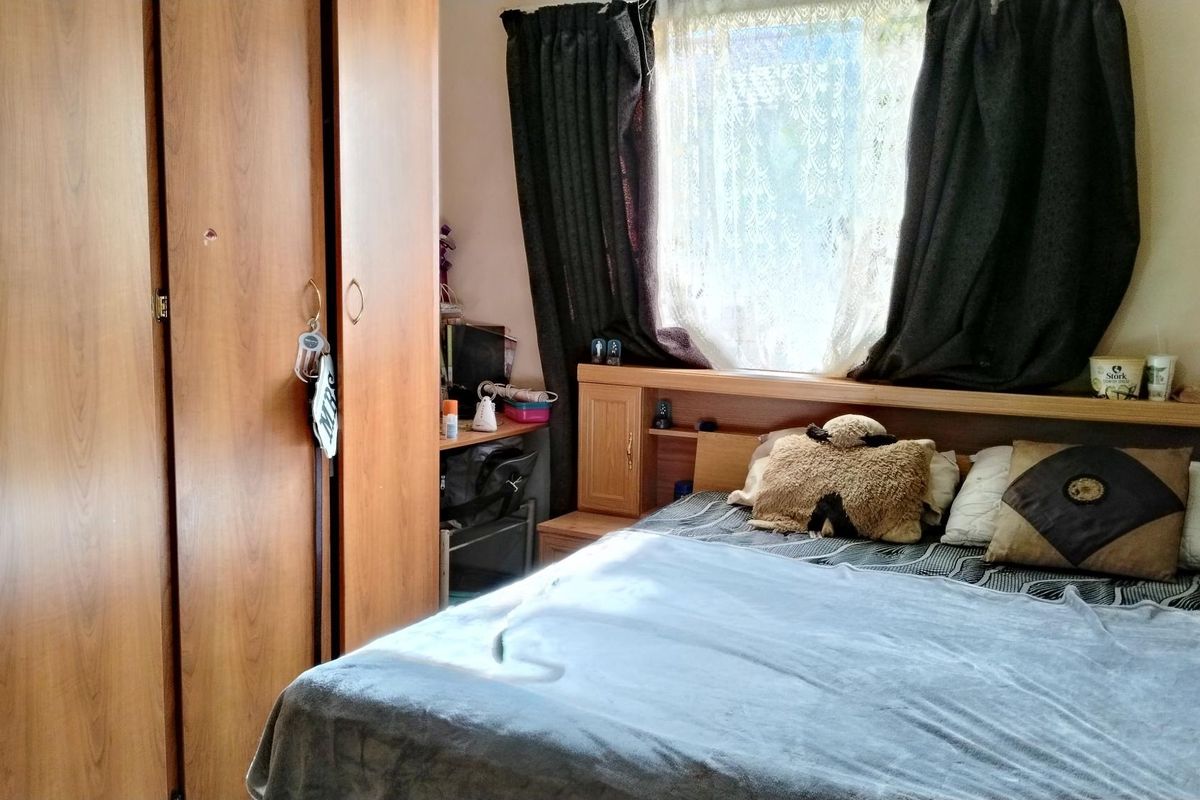 A bedroom featuring a built-in wooden wardrobe and a matching integrated headboard with storage shelving.