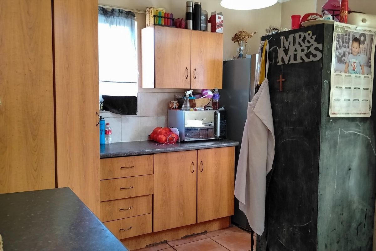 A functional kitchen featuring wood-look laminate cabinetry, dark countertops, and tiled flooring, offering a practical layout with potential for cosmetic updates.