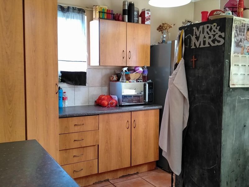 A functional kitchen featuring wood-look laminate cabinetry, dark countertops, and tiled flooring, offering a practical layout with potential for cosmetic updates.