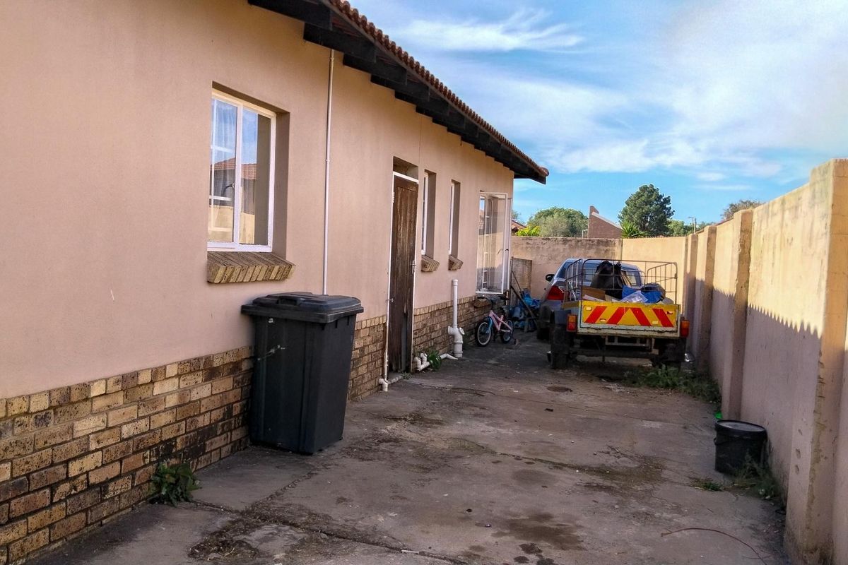 Rear exterior view of the property featuring a concrete driveway, brick boundary wall, and plastered facade with tiled roof.