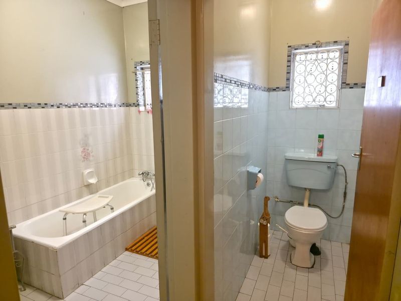 A functional bathroom featuring a built-in bathtub and separate toilet area with tiled finishes and security bars on the windows.