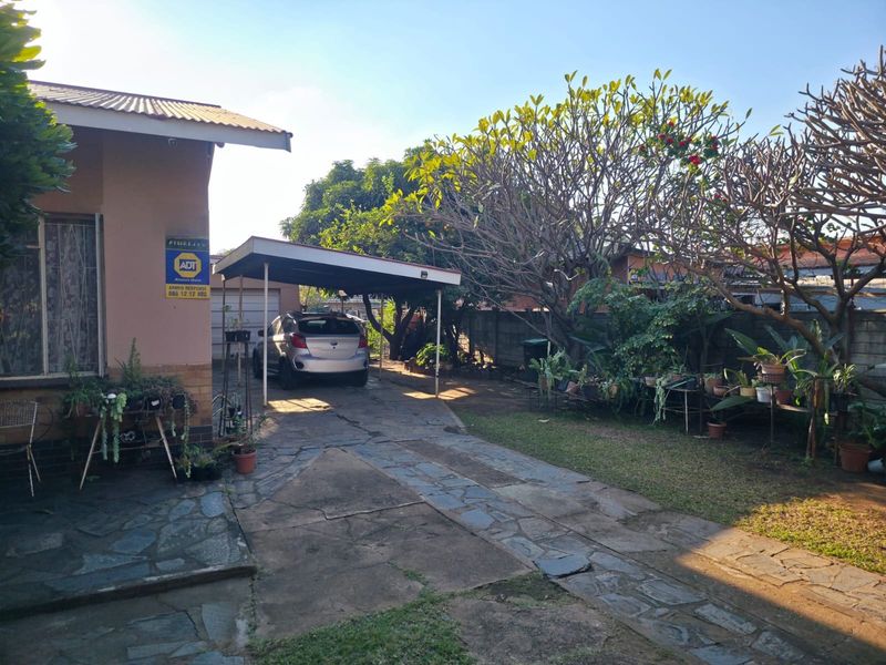 Front exterior view featuring a paved driveway, a covered carport, and established garden landscaping alongside the property boundary wall.