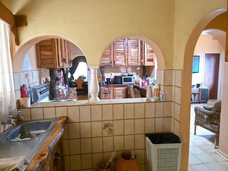 Kitchen featuring rustic wooden cabinetry, tiled splashbacks, and a stainless steel sink, connected to the living area through distinctive arched wall openings.