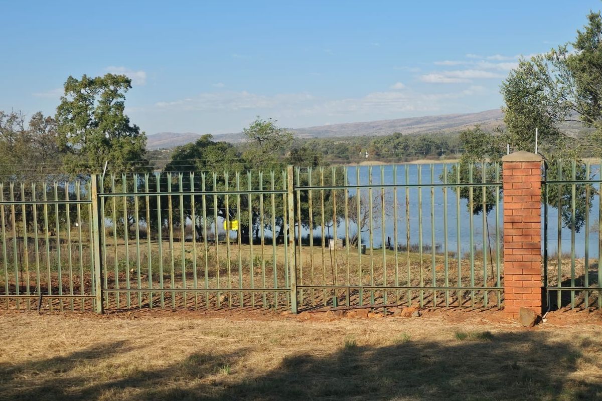 A view of the rear boundary featuring metal palisade fencing with a brick pillar, overlooking a scenic lake and natural landscape.