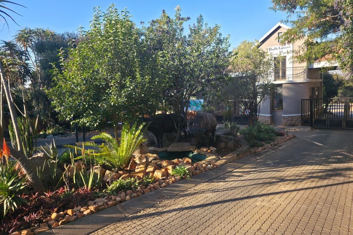 Entrance view of the residential estate featuring a paved driveway, landscaped garden, and secure gated access.
