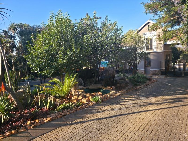 Entrance view of the residential estate featuring a paved driveway, landscaped garden, and secure gated access.