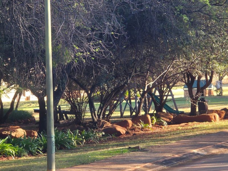 A well-maintained garden area featuring mature trees, natural rock landscaping, and integrated playground equipment.