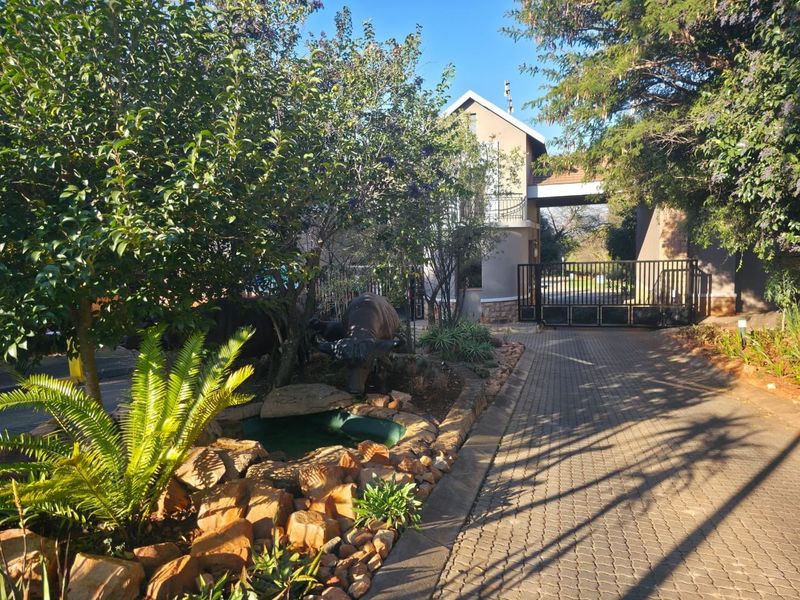 Front entrance view featuring a paved driveway, metal security gate, and landscaped garden area with a small water feature.