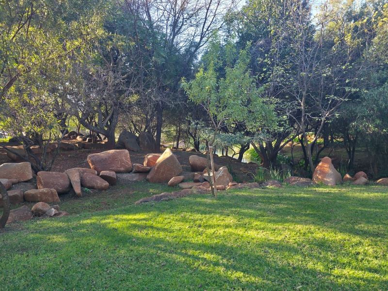 A well-maintained residential garden featuring a lush green lawn, mature trees, and natural rock landscaping elements.