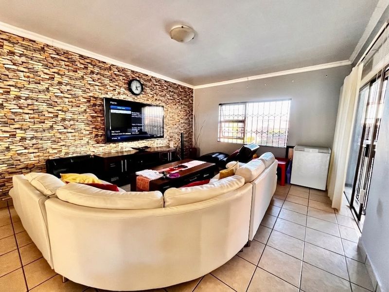 A living room featuring a stone veneer accent wall, ceramic tiled flooring, and large sliding glass doors providing access to the exterior.