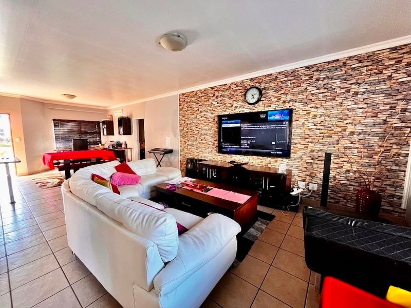 Spacious open-plan living area featuring a prominent stone veneer feature wall, ceramic tiled flooring, and integrated lighting throughout the combined living and dining space.