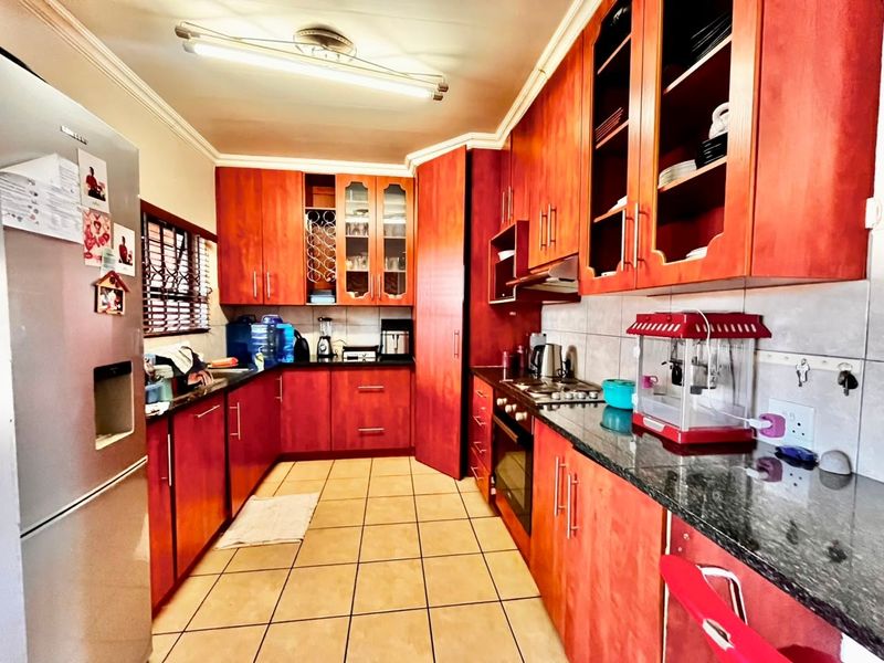 A functional kitchen featuring warm-toned wooden cabinetry, granite countertops, built-in oven, and hob, with tiled flooring and ample storage space.