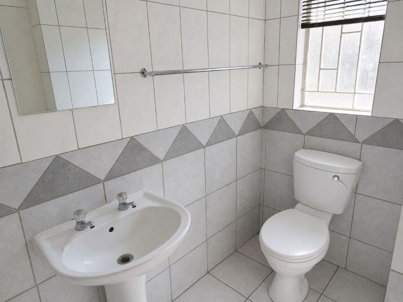 A functional bathroom featuring a pedestal basin, toilet, and neutral tiled finishes with a decorative border.