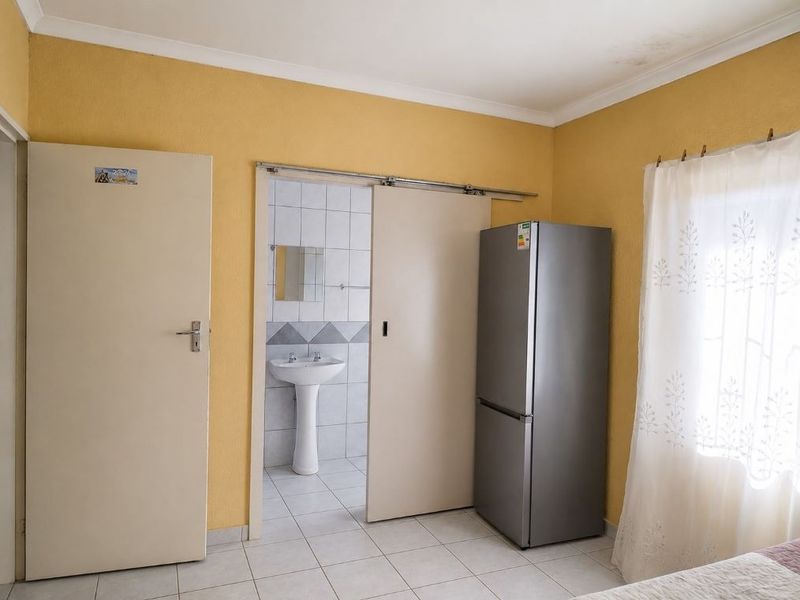 A bedroom featuring tiled flooring and an en-suite bathroom with a pedestal basin, showing some signs of ceiling water staining.