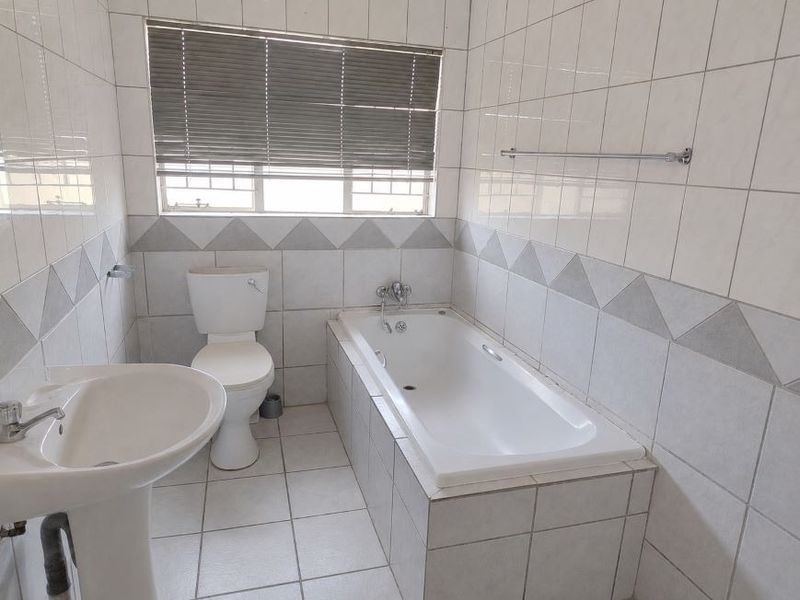A functional bathroom featuring a pedestal basin, toilet, and a built-in bathtub with tiled walls and flooring.