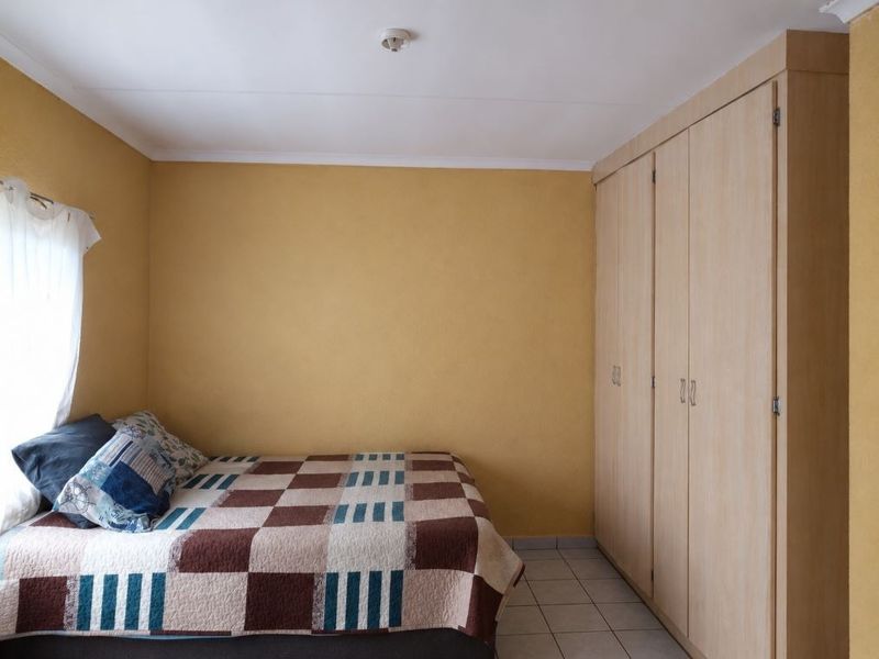 A bedroom featuring built-in wooden cupboards, tiled flooring, and a neutral yellow wall finish.