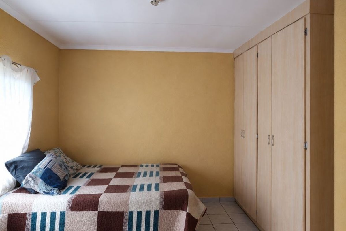 A bedroom featuring built-in wooden cupboards, tiled flooring, and a neutral yellow wall finish.