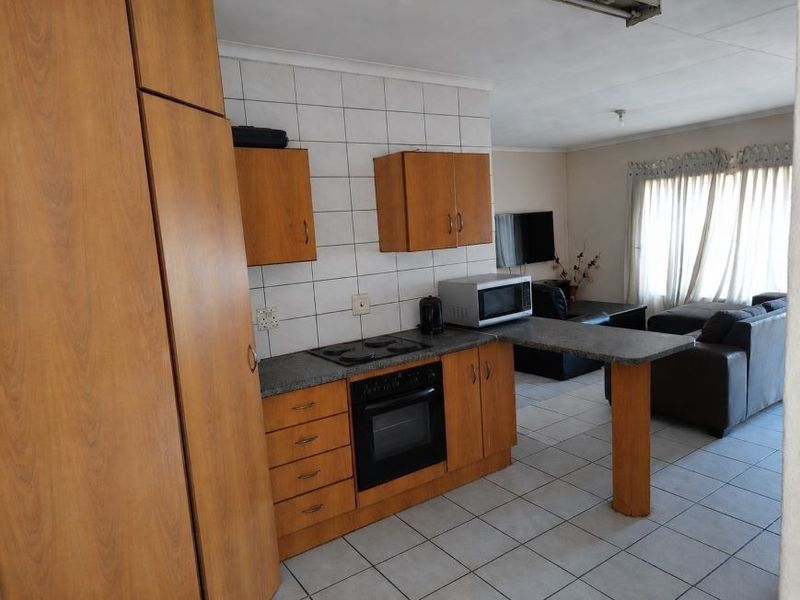 Open plan kitchen and living area featuring wooden cabinetry, built-in oven and hob, breakfast bar, and tiled flooring throughout.