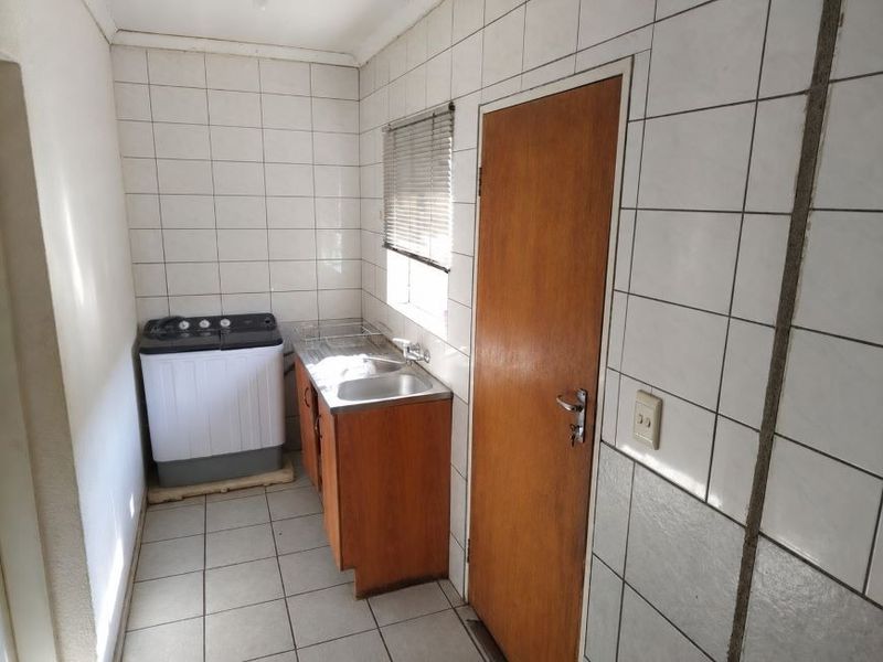 A functional laundry area featuring tiled walls, a stainless steel sink, and built-in cabinetry, providing a practical space for washing and utility tasks.