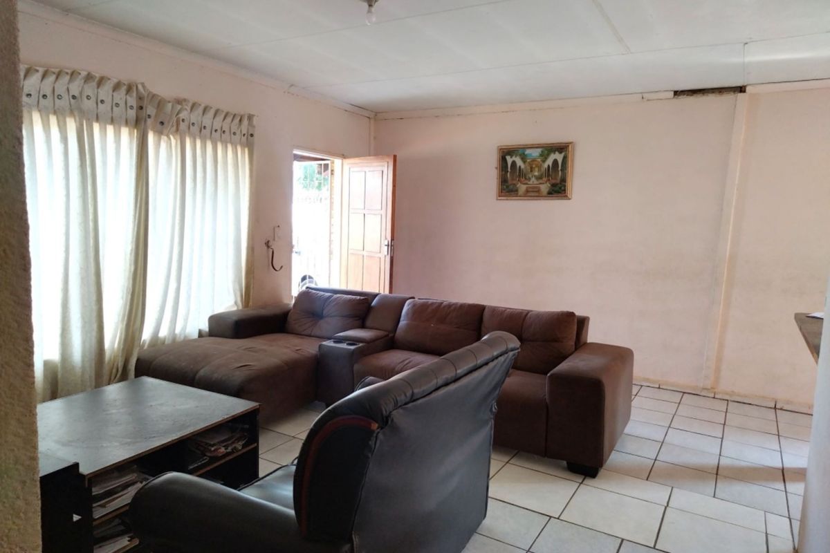 A living room featuring ceramic floor tiles and direct access to an exterior door, requiring cosmetic updates to the walls and ceiling.