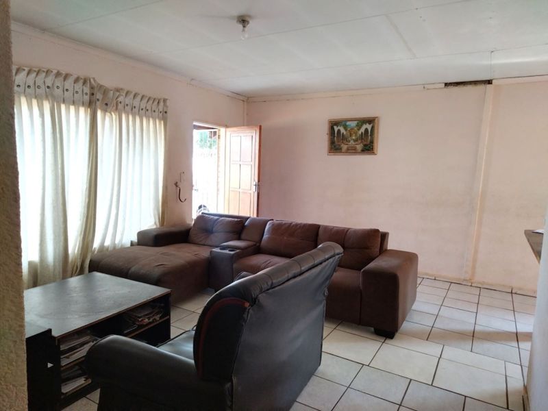 A living room featuring ceramic floor tiles and direct access to an exterior door, requiring cosmetic updates to the walls and ceiling.