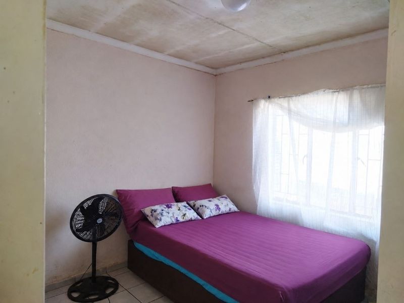 A compact bedroom featuring tiled flooring and a window fitted with security bars, requiring cosmetic updates to the ceiling and walls.