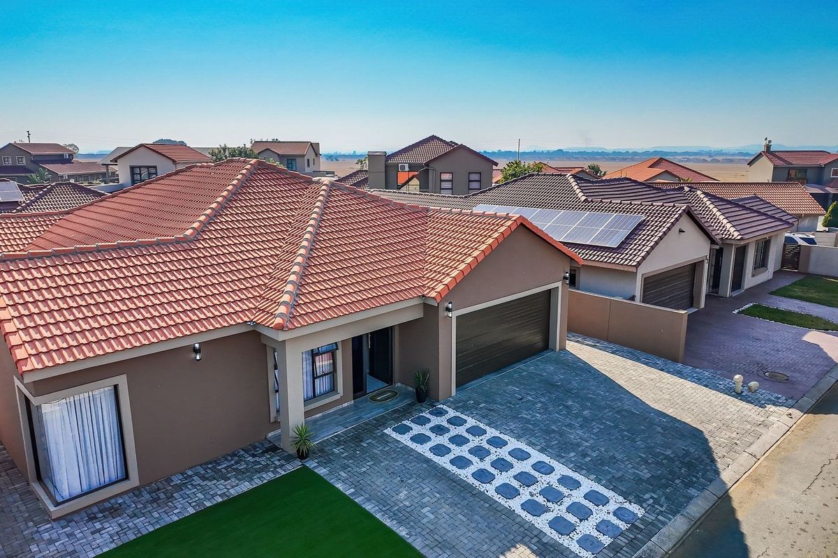 Aerial view of a modern residential property featuring a tiled roof, solar panels, and a paved driveway in a well-maintained estate setting.