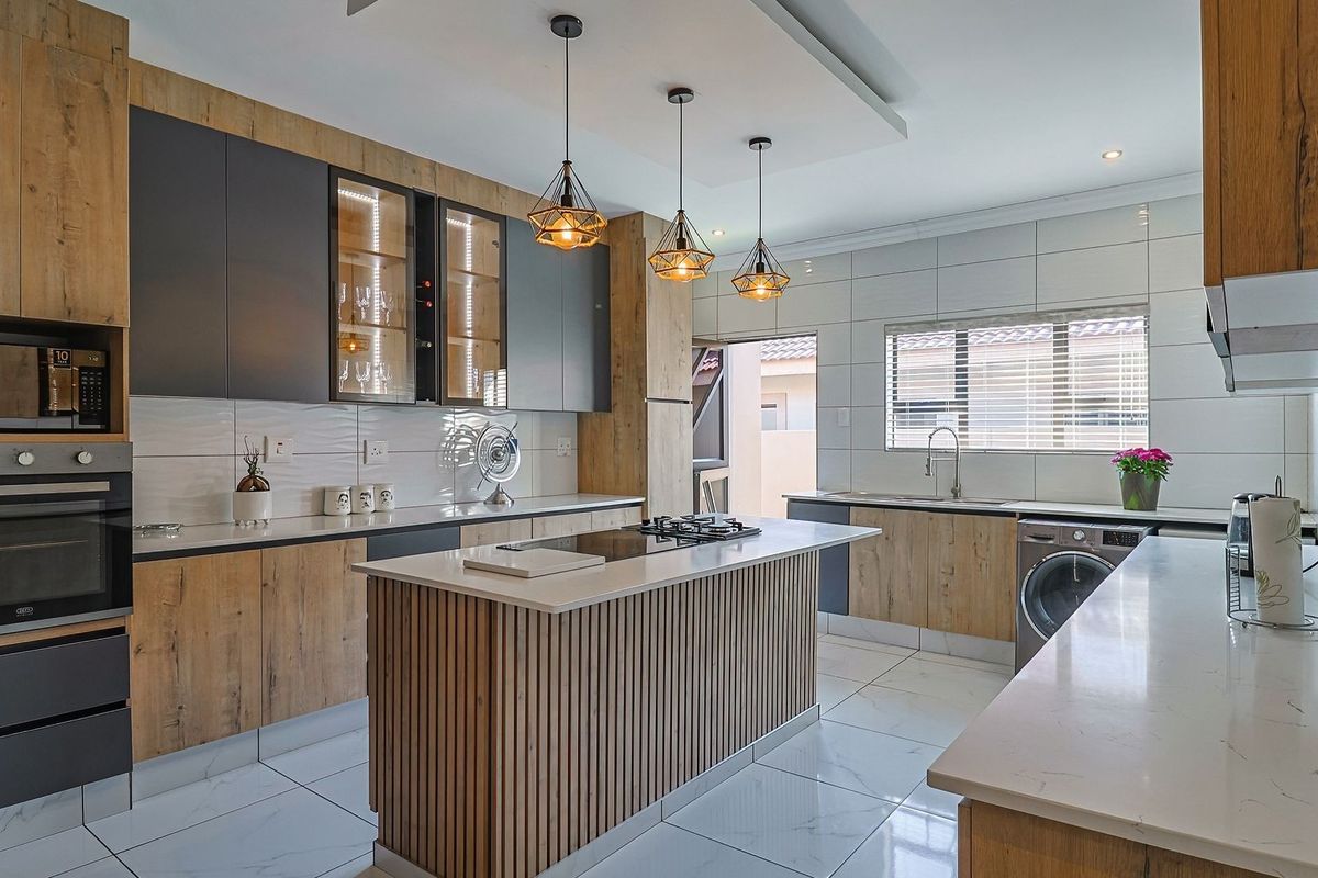 Modern kitchen featuring wood-grain and matte grey cabinetry, stone countertops, a central island with hob, and high-end built-in appliances.