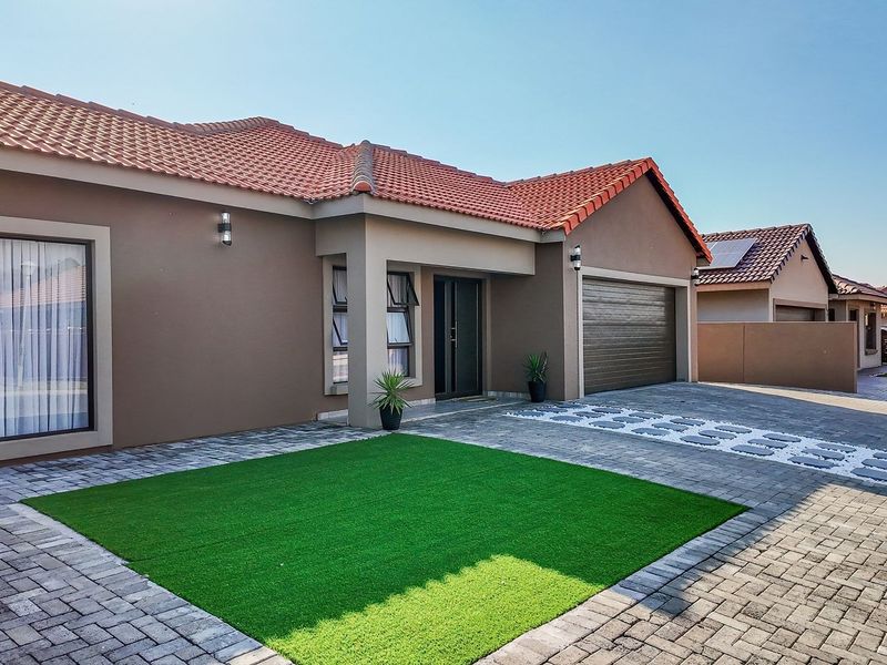 A well-maintained modern single-story home featuring a tiled roof, paved driveway, integrated garage, and neat artificial lawn in the front garden area.