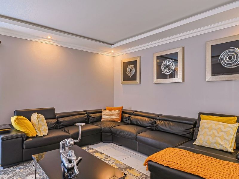A well-maintained living room featuring neutral wall tones, crown molding, recessed ceiling lighting, and polished tile flooring.