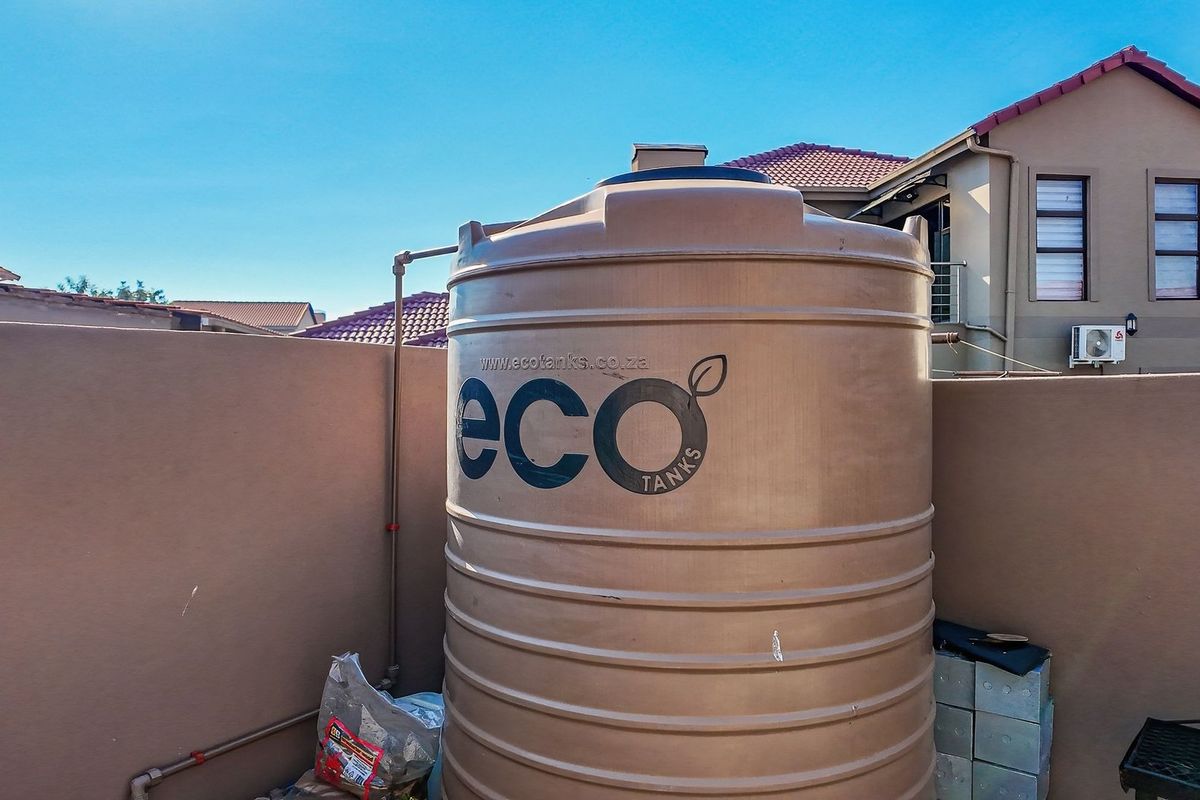 A residential exterior area featuring a large plastic water storage tank installed against a boundary wall.