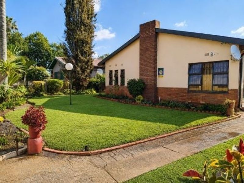 Front view of a single-story house featuring a brick chimney, a well-maintained lawn, and a paved driveway.