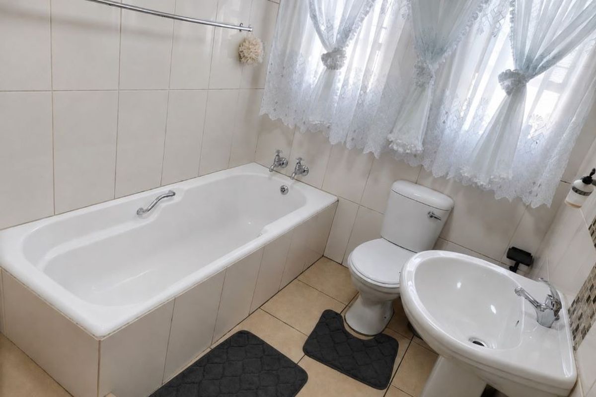 A functional bathroom featuring a built-in bathtub, pedestal washbasin, and toilet, finished with neutral ceramic wall and floor tiles.