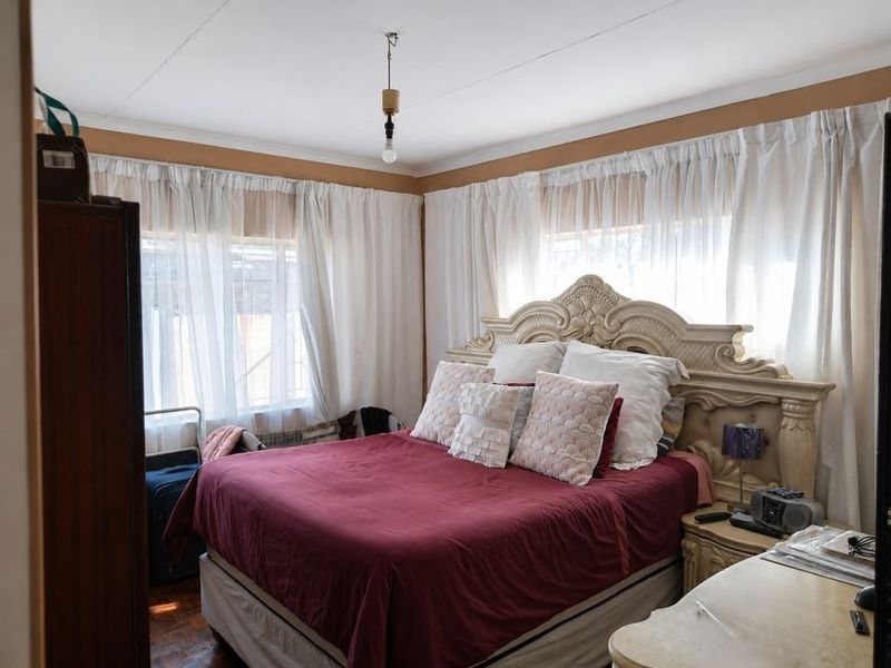 A bedroom featuring parquet flooring, coved ceilings, and natural light through large windows with curtains.