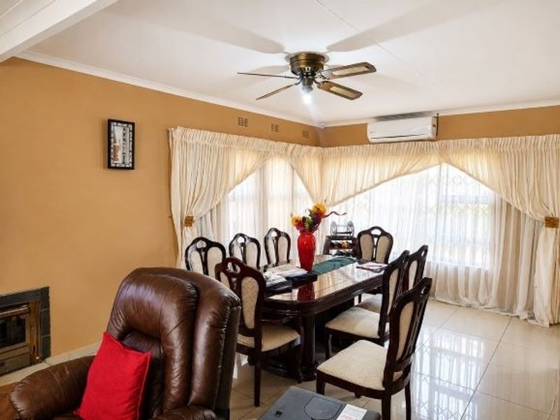 A dining room featuring tiled flooring, a ceiling fan, a wall-mounted air conditioner, and a built-in fireplace.