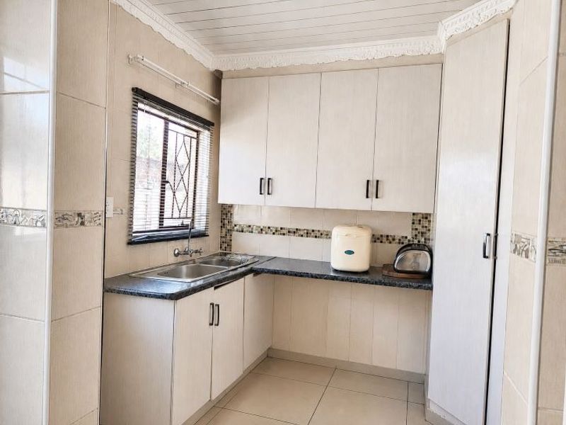 A functional kitchen featuring light-toned cabinetry, a double sink, tiled splashbacks, and tiled flooring with decorative wall accents.